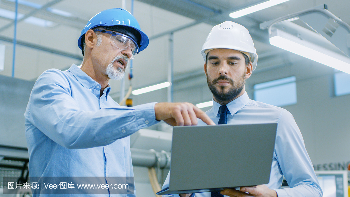 部門主管持有筆記本電腦并與總工程師討論產(chǎn)品細節(jié)。他們戴著安全帽在現(xiàn)代工廠工作。